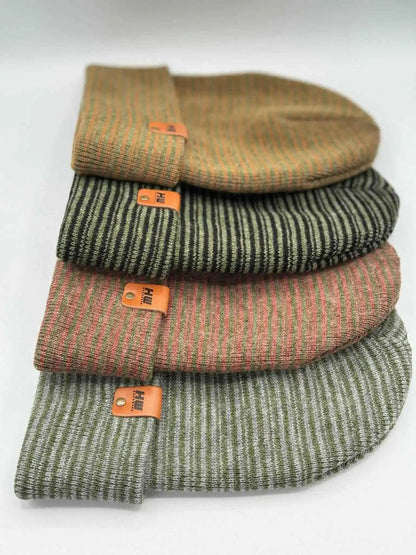 Stack of knit beanies with folded cuffs and orange logo patches, gray-green tones