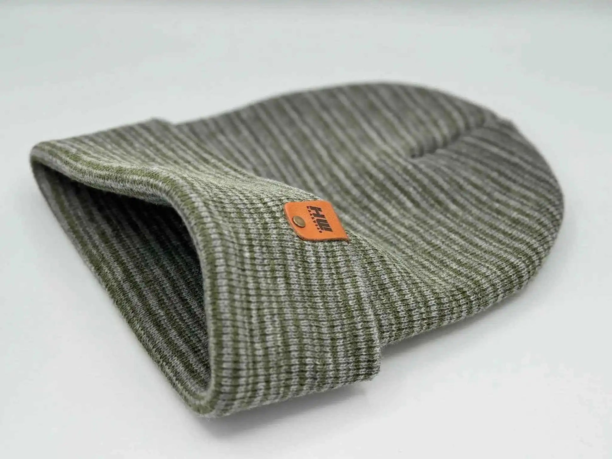 Gray-green knit beanie with folded cuff, side view, orange logo patch