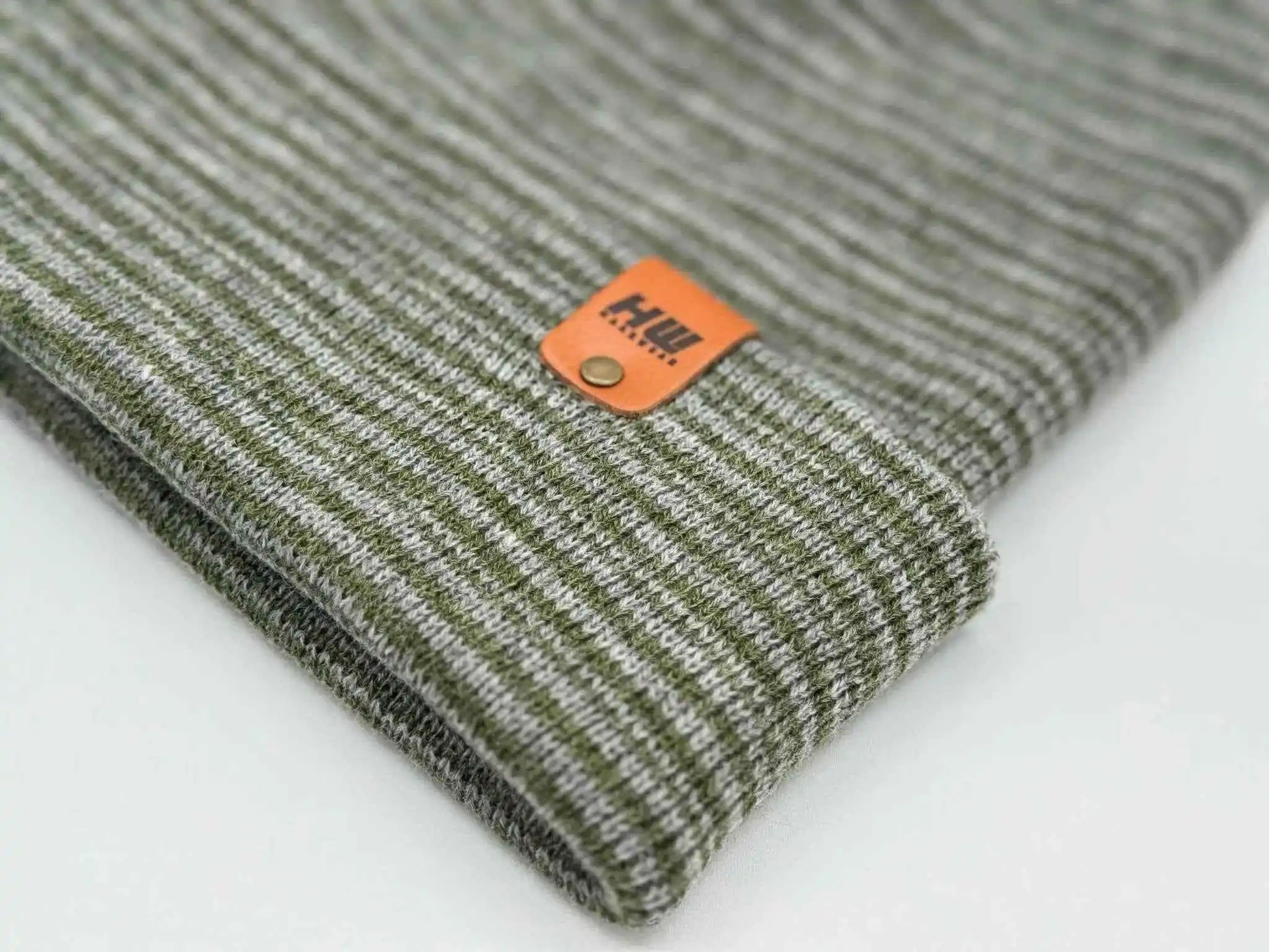 Gray-green knit beanie folded cuff close-up with orange logo patch