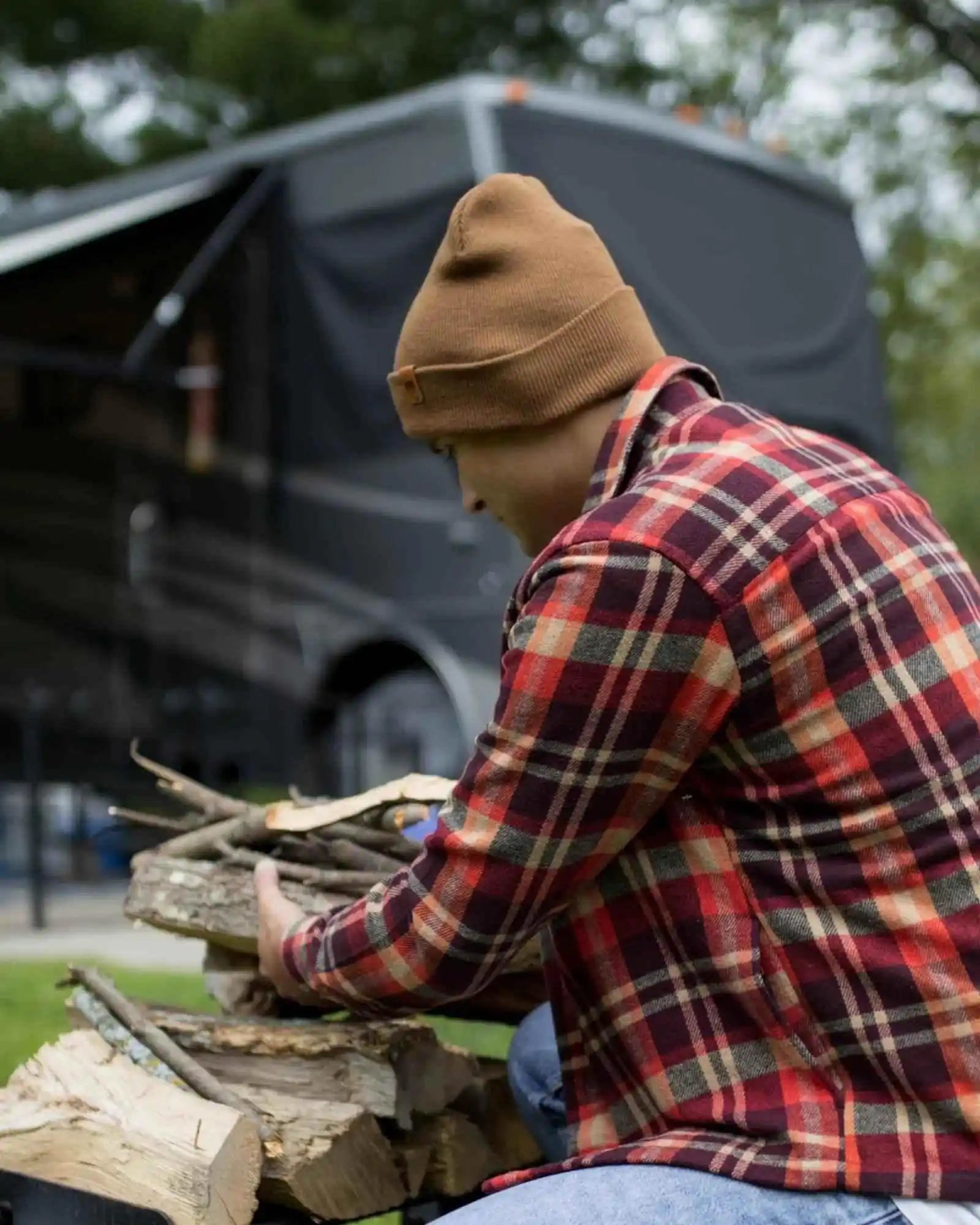 Camel brown cuffed beanie with side logo patch, worn while carrying firewood