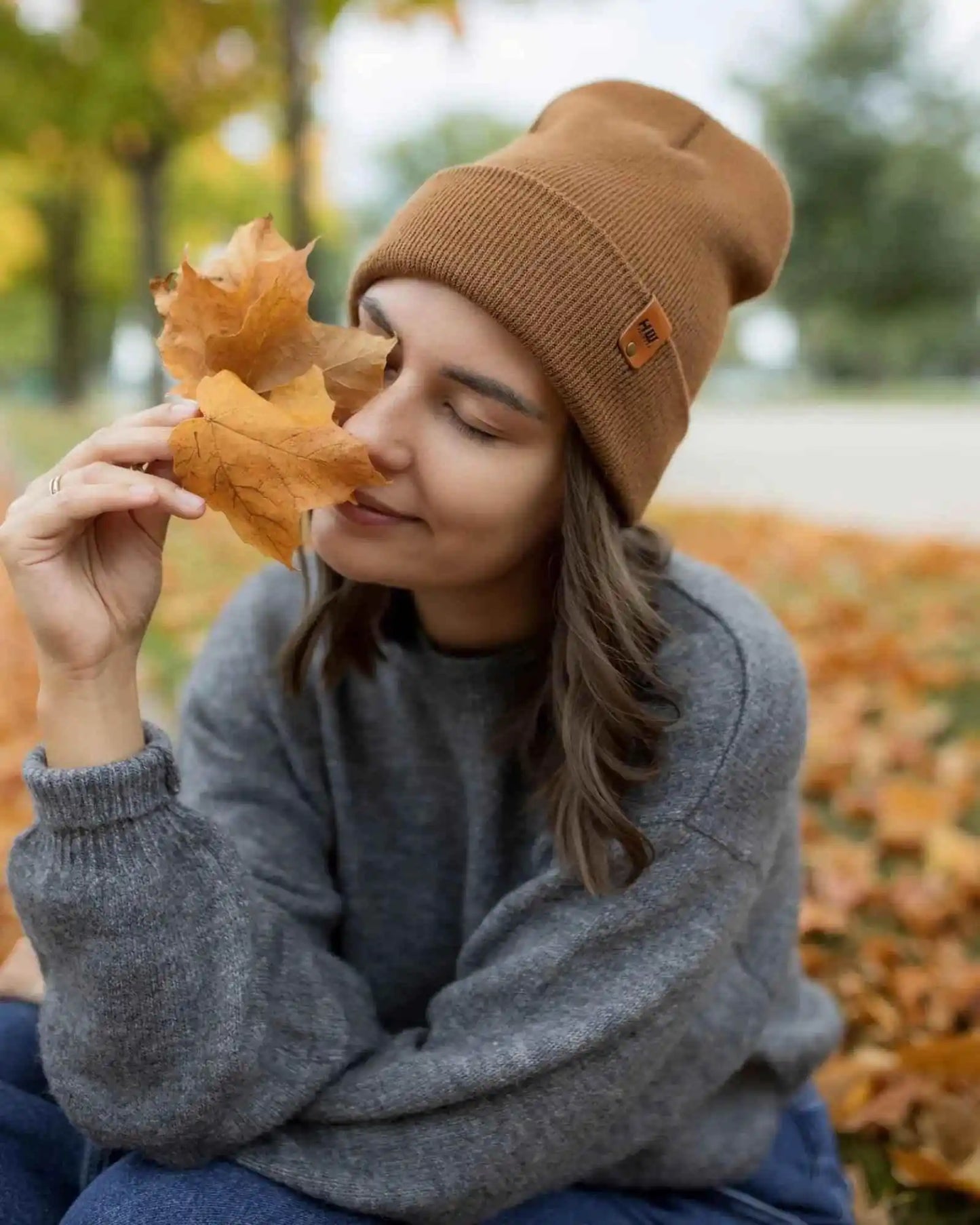 Camel brown beanie with folded cuff and logo patch, near autumn leaves