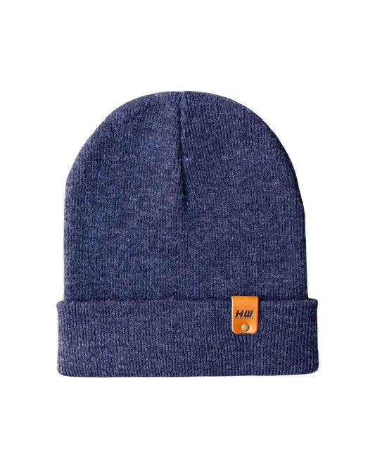 Denim blue knit beanie with folded cuff and small tan logo patch