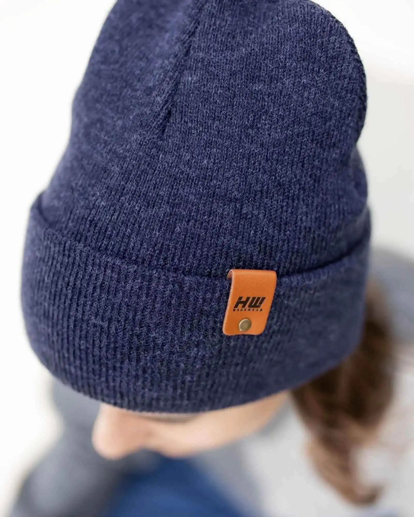 Denim blue knit beanie with folded cuff and tan leather-look logo patch