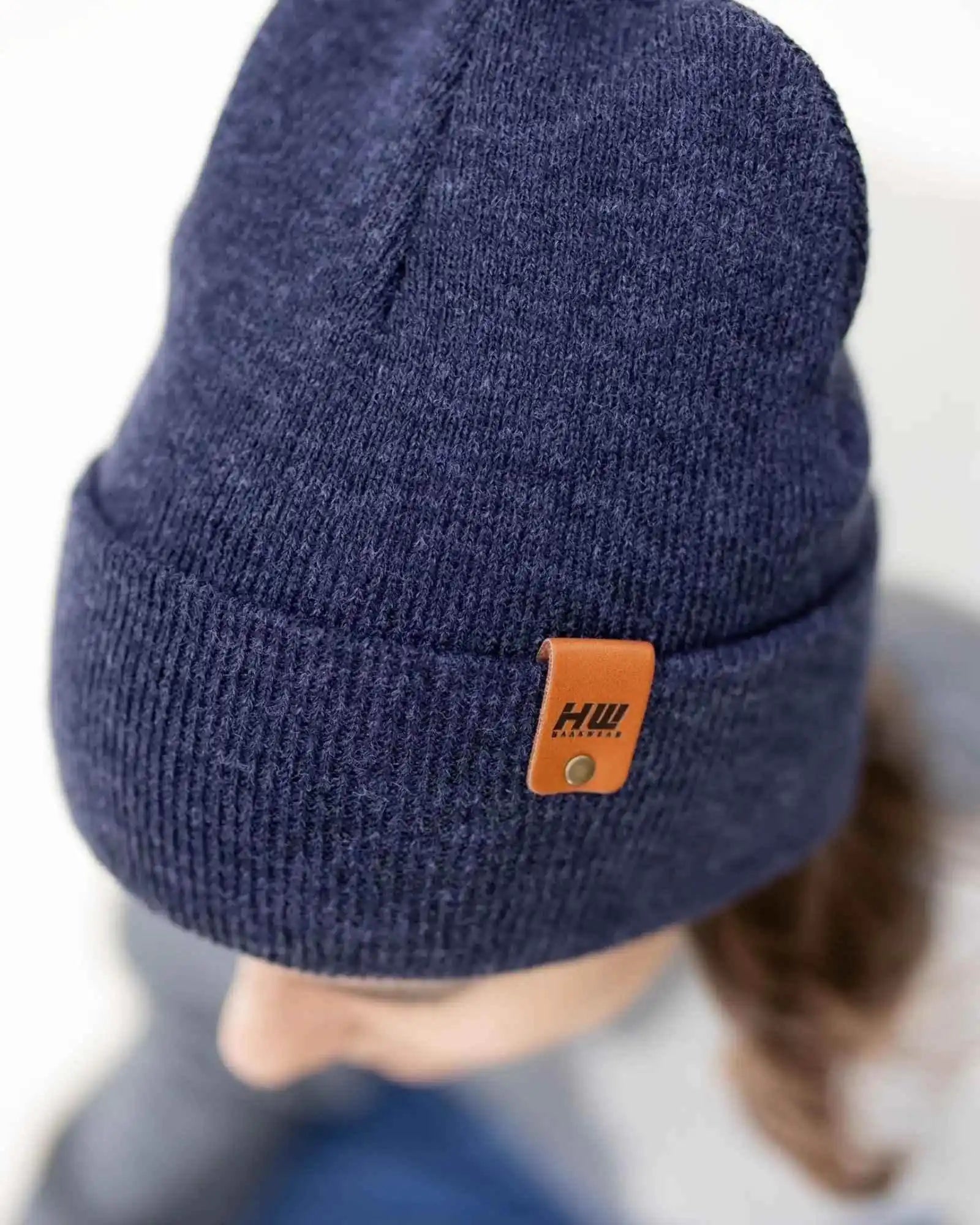 Denim blue knit beanie with folded cuff and tan leather-look logo patch