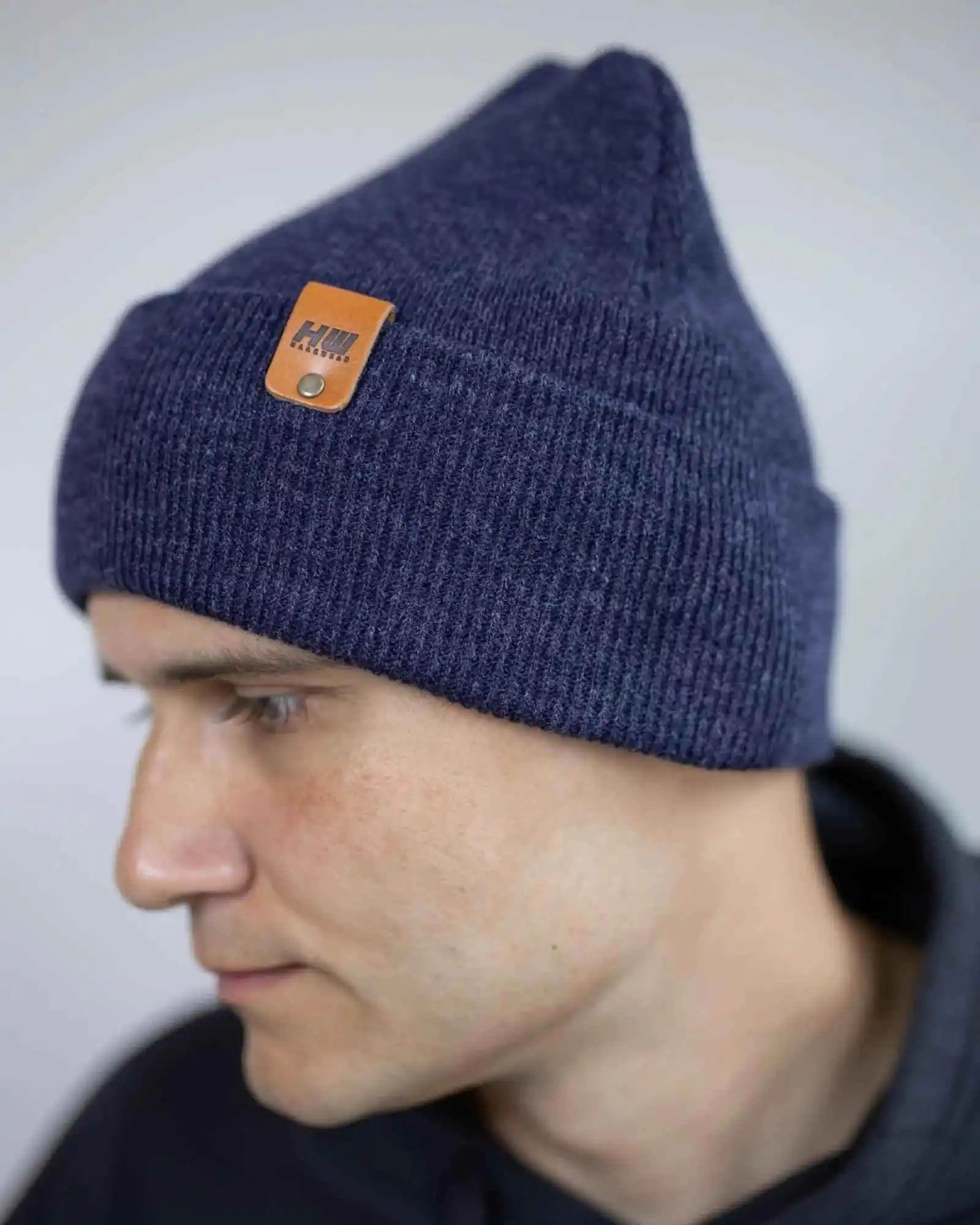 Denim blue knit beanie with tan logo patch near folded cuff