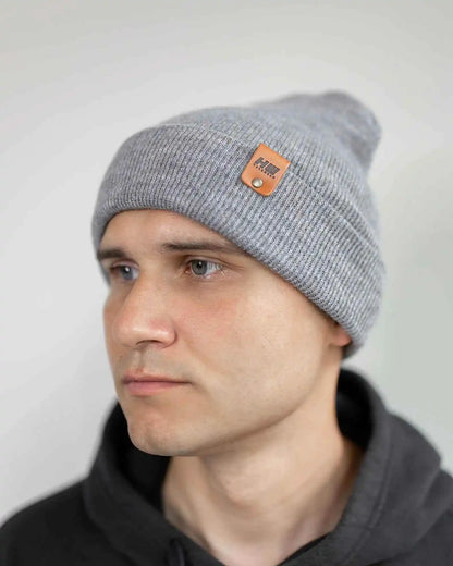 Gray knit beanie on person, side view with folded cuff and brown logo patch