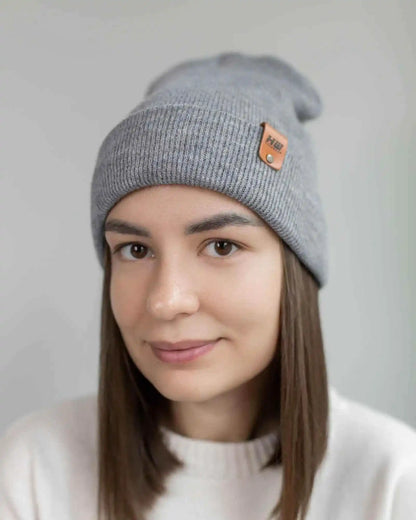 Gray knit beanie on person, folded cuff and brown logo patch at side