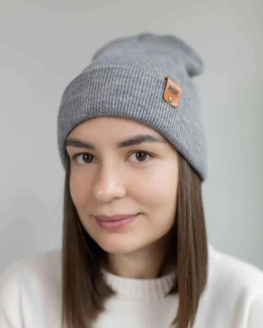 Gray knit beanie on person, folded cuff and brown logo patch at side