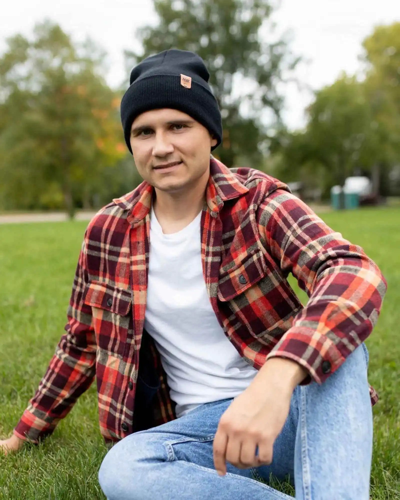 Dark beanie with fold-over cuff and orange logo patch, worn with plaid shirt