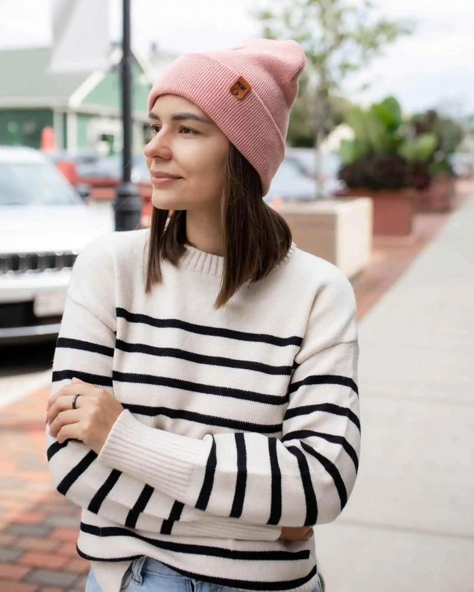 Pearl pink ribbed beanie with folded cuff and logo patch, worn on head.