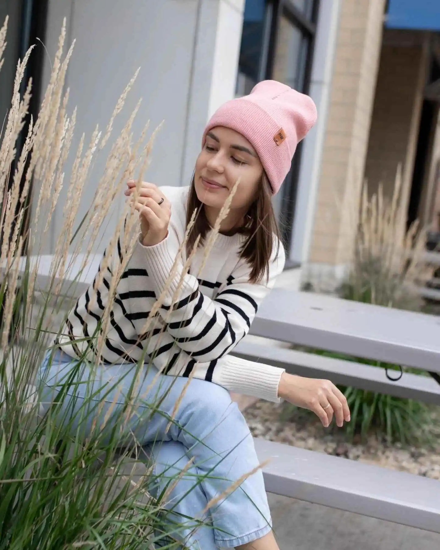 Pearl pink ribbed cuff beanie with folded brim and small logo patch, worn outdoors.