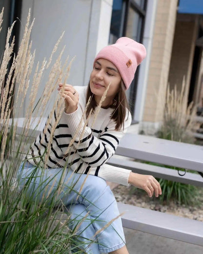 Pearl pink ribbed cuff beanie with folded brim and small logo patch, worn outdoors.