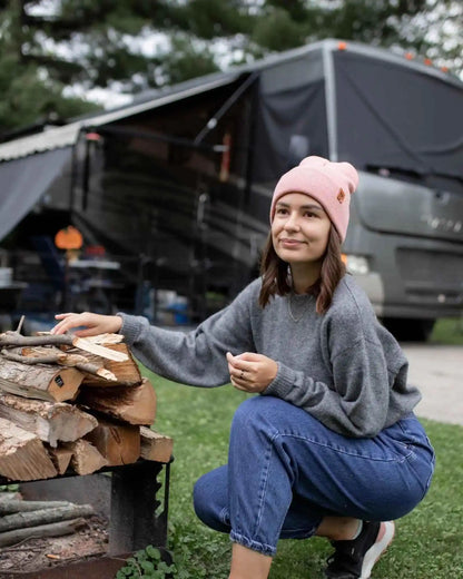 Pearl pink knit beanie with folded cuff and small logo patch, worn on head outdoors.