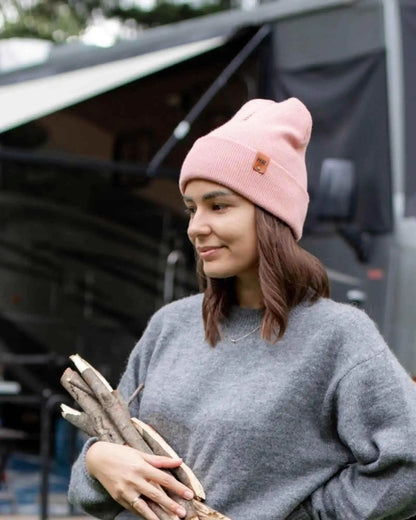 Pearl pink knit beanie with folded cuff and logo patch, worn on head.