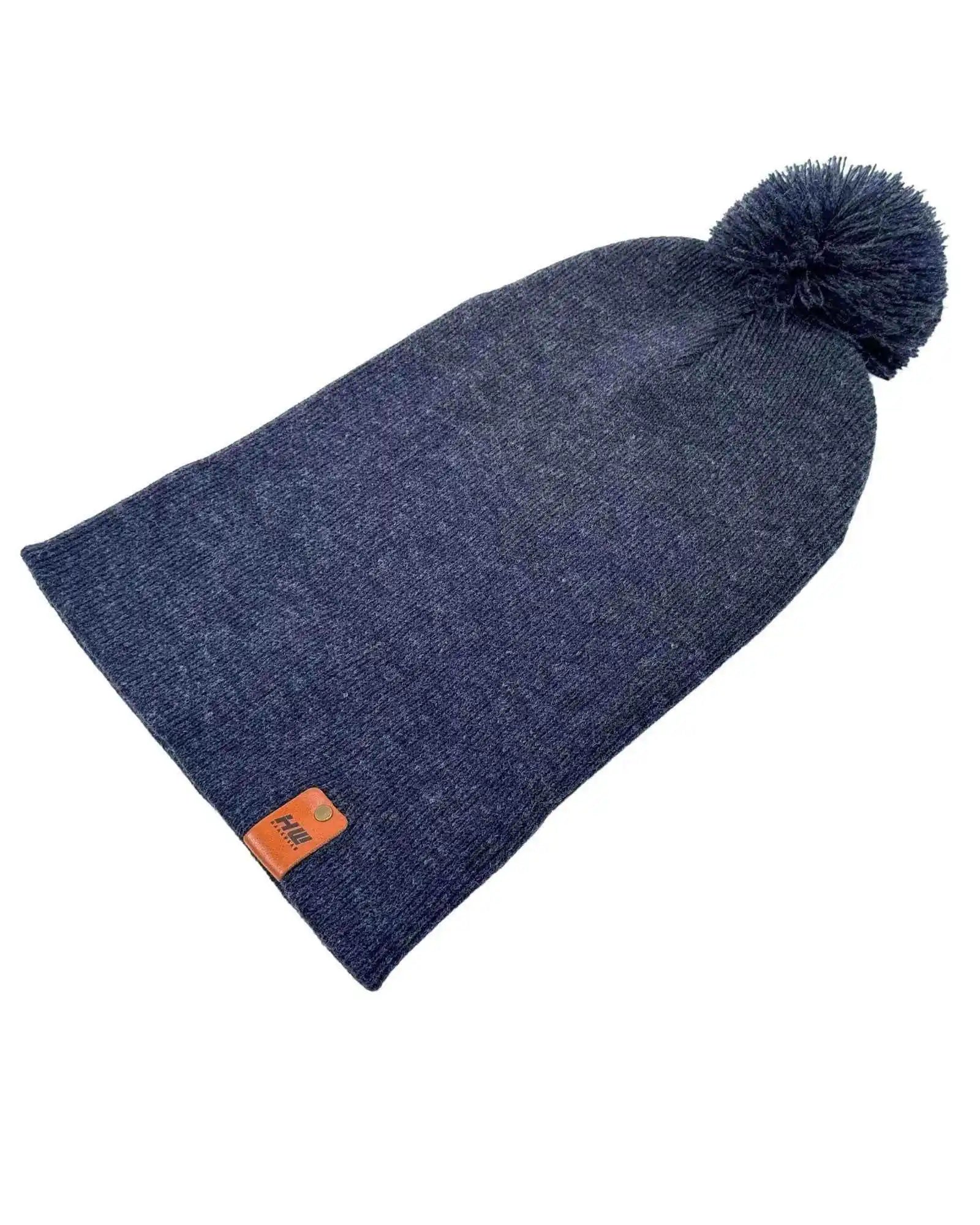 Denim blue knit beanie with pom pom and folded cuff, orange rectangular logo patch