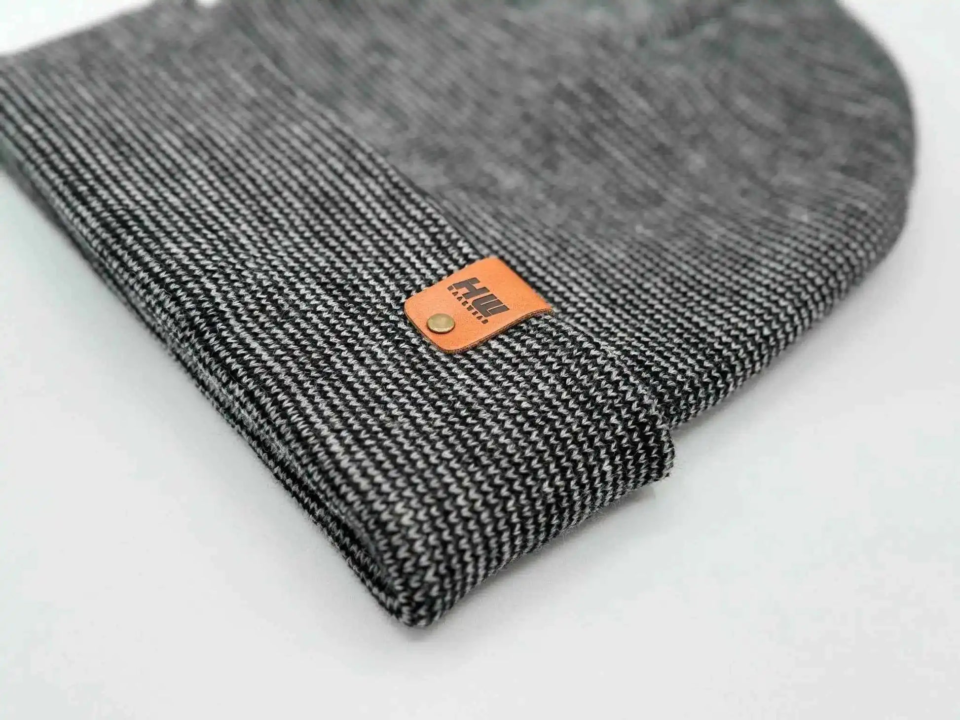 Cuffed beanie corner close-up with orange logo patch on dark gray knit