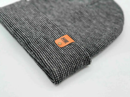 Cuffed beanie corner close-up with orange logo patch on dark gray knit