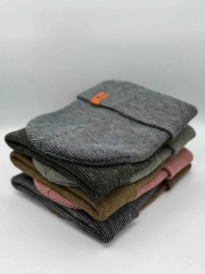 Stacked cuffed beanies in gray and darker tones with orange logo patch