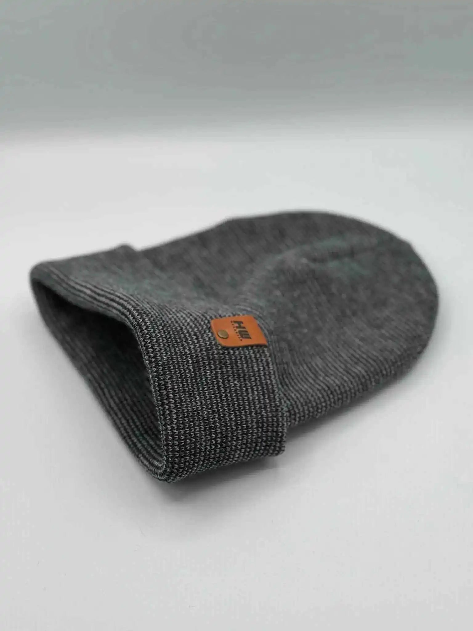 Gray knit cuffed beanie folded flat, featuring an orange square logo patch