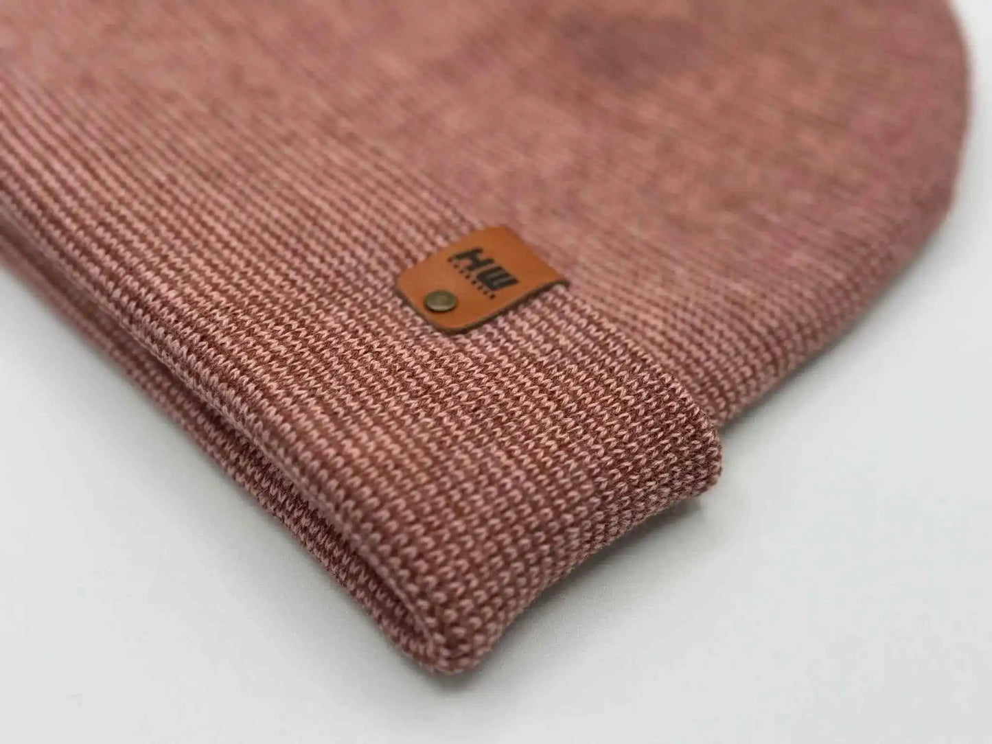 Close-up burgundy-pink ribbed knit beanie with tan leather logo patch