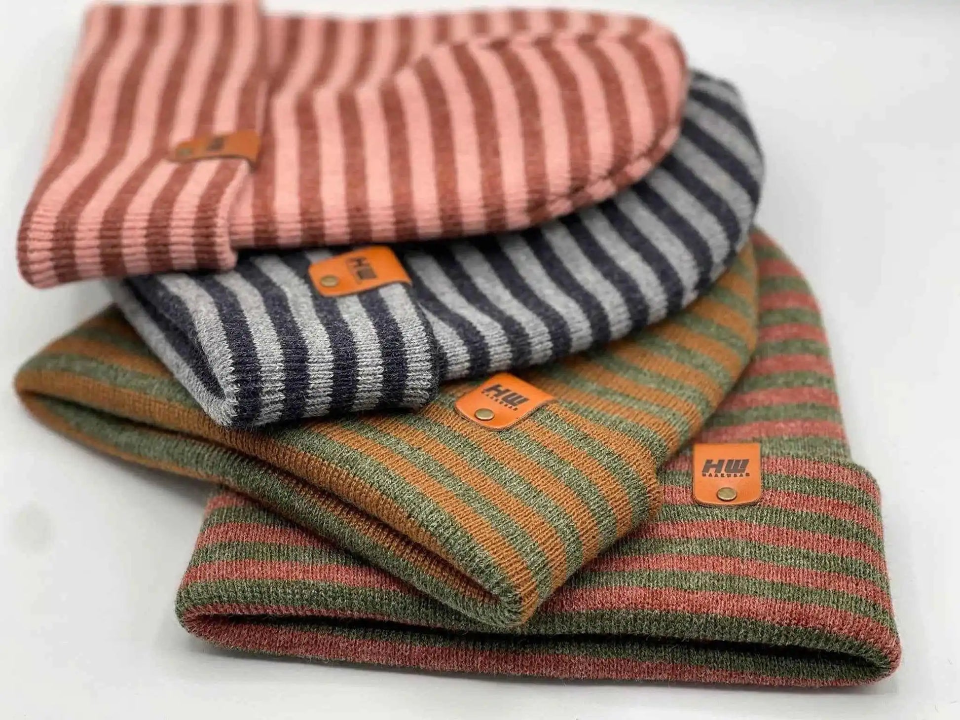 Stack of striped beanies with cuffs and logo patches in burgundy, green, and navy