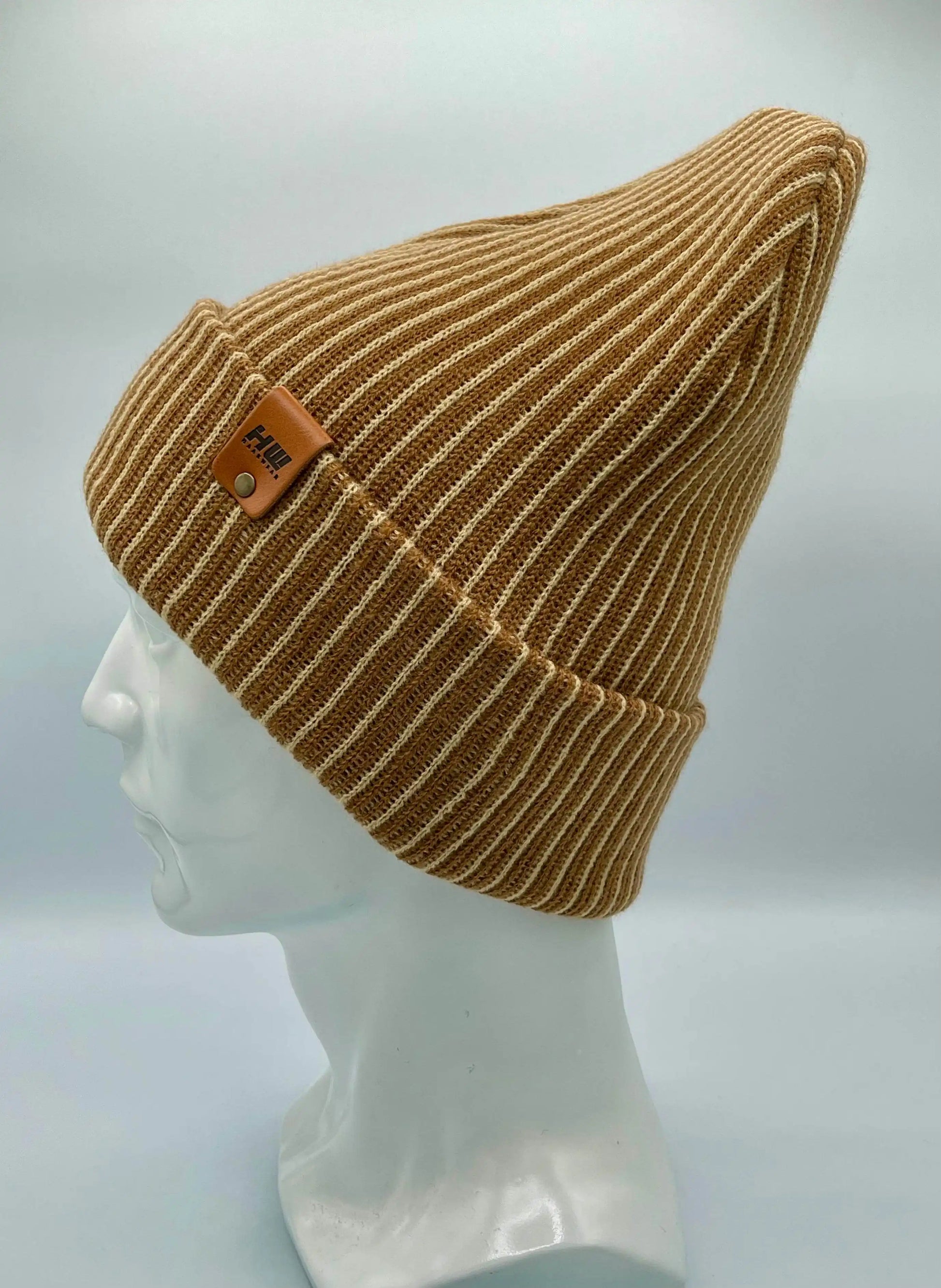 Beige and brown striped rib-knit beanie on head form, folded cuff, leather logo patch