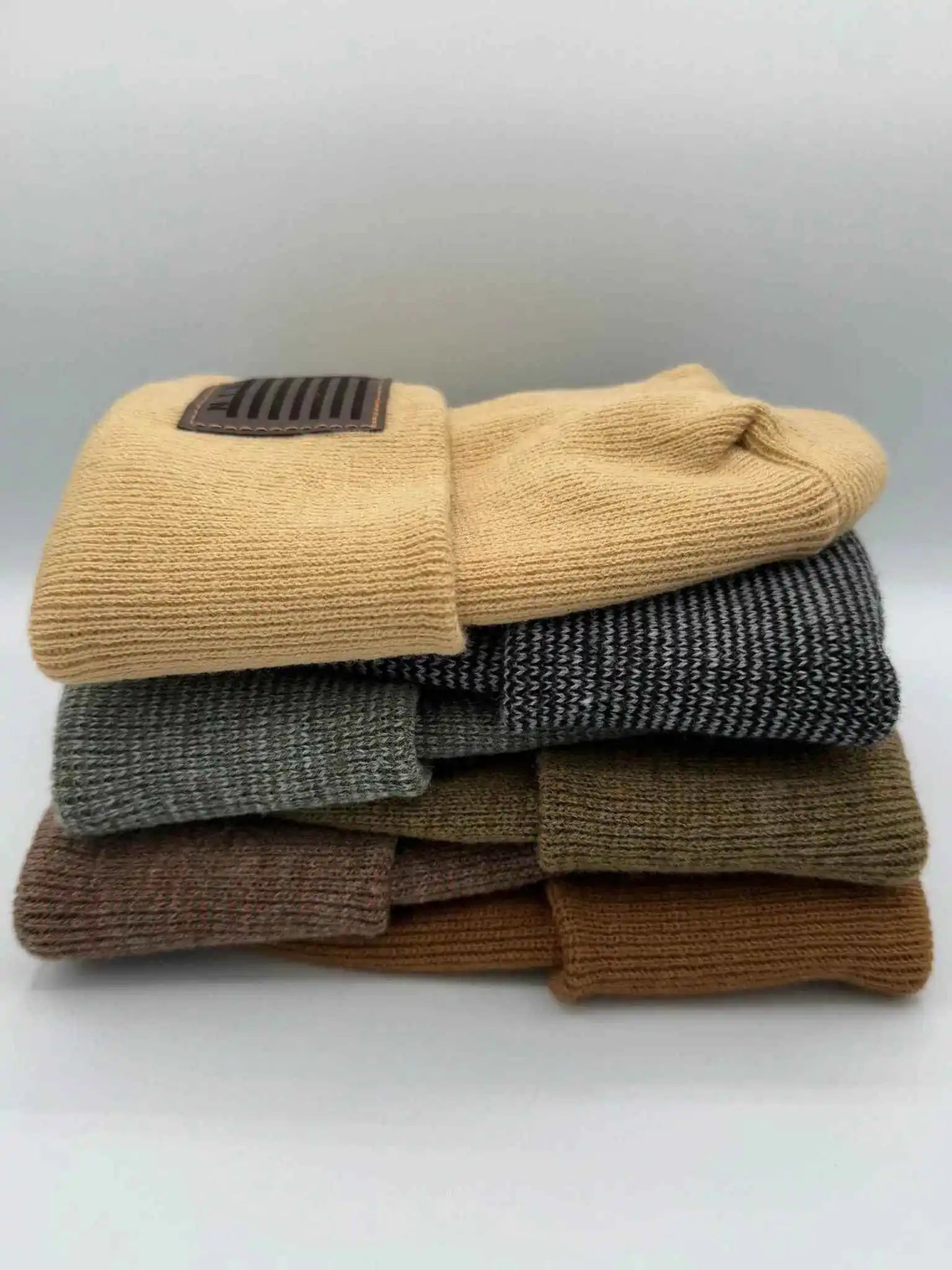 Stacked cuffed knit beanies in beige, heather gray, olive, and brown with Veterans patches