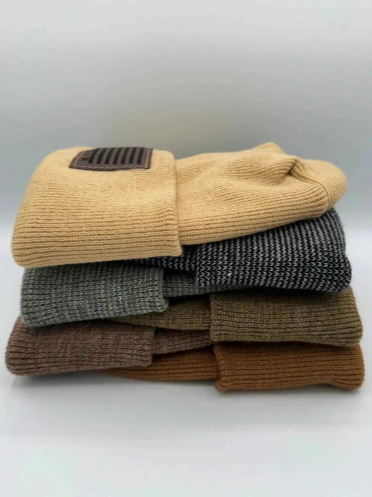 Stacked cuffed knit beanies in beige, heather gray, olive, and brown with Veterans patches
