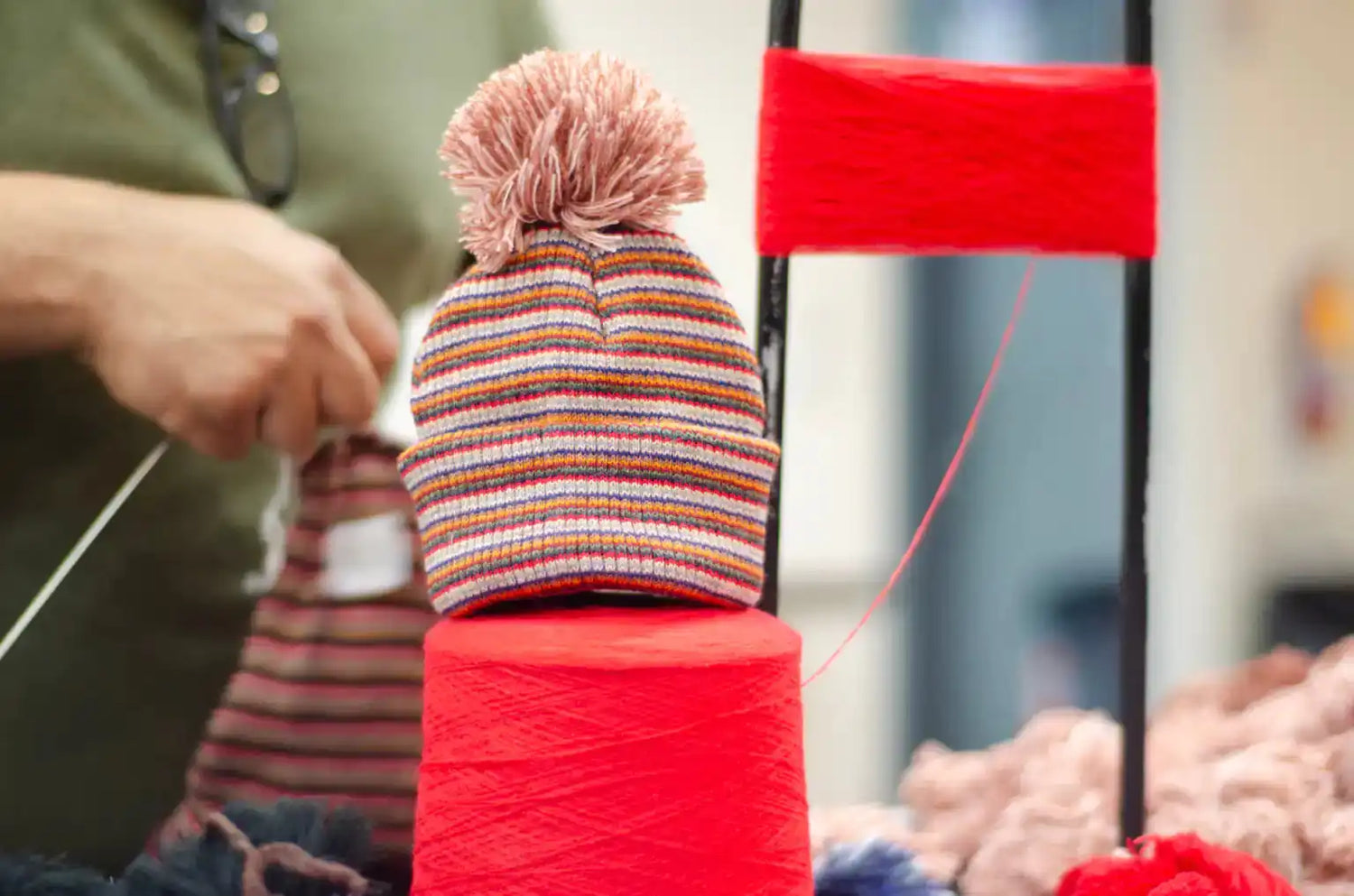 Colorful knitted hat on a red yarn spool with blurred background showing how haakwear beanies are made.