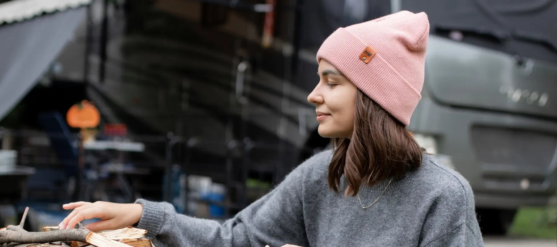 a model wearing a pink beanie while building a fire and camping with a haakwear winter hat