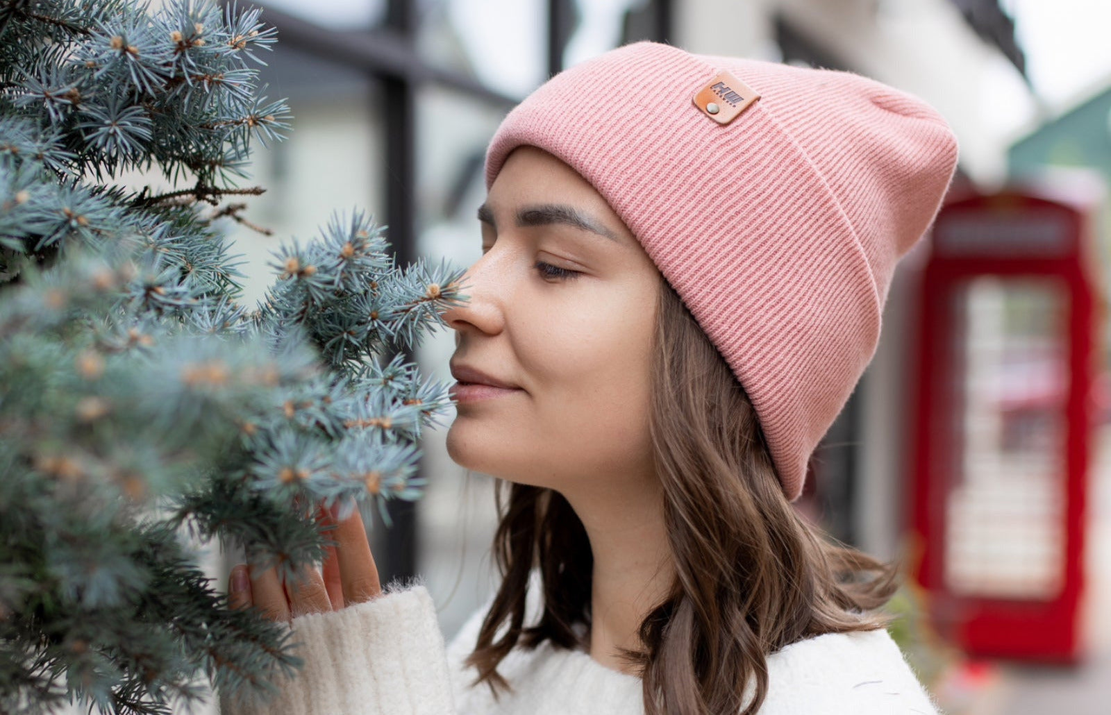 Woman wearing a pink beanie and white sweater standing next to a tree