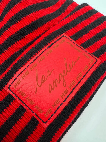 Close-up of striped black and red beanie knit with red logo patch detail