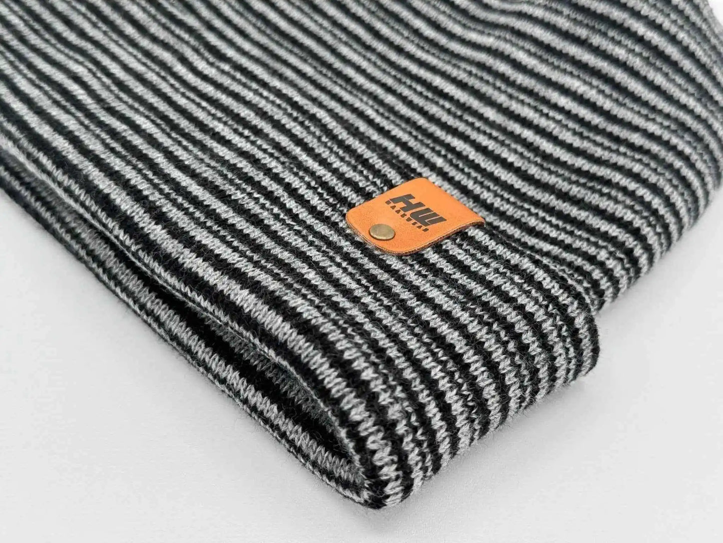 Black and gray striped knit beanie with orange logo patch (folded)
