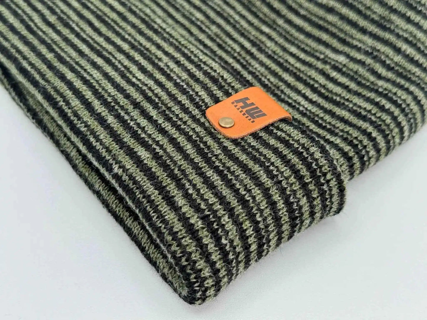 Striped beanie cuff close-up with orange logo patch, green and dark gray knit