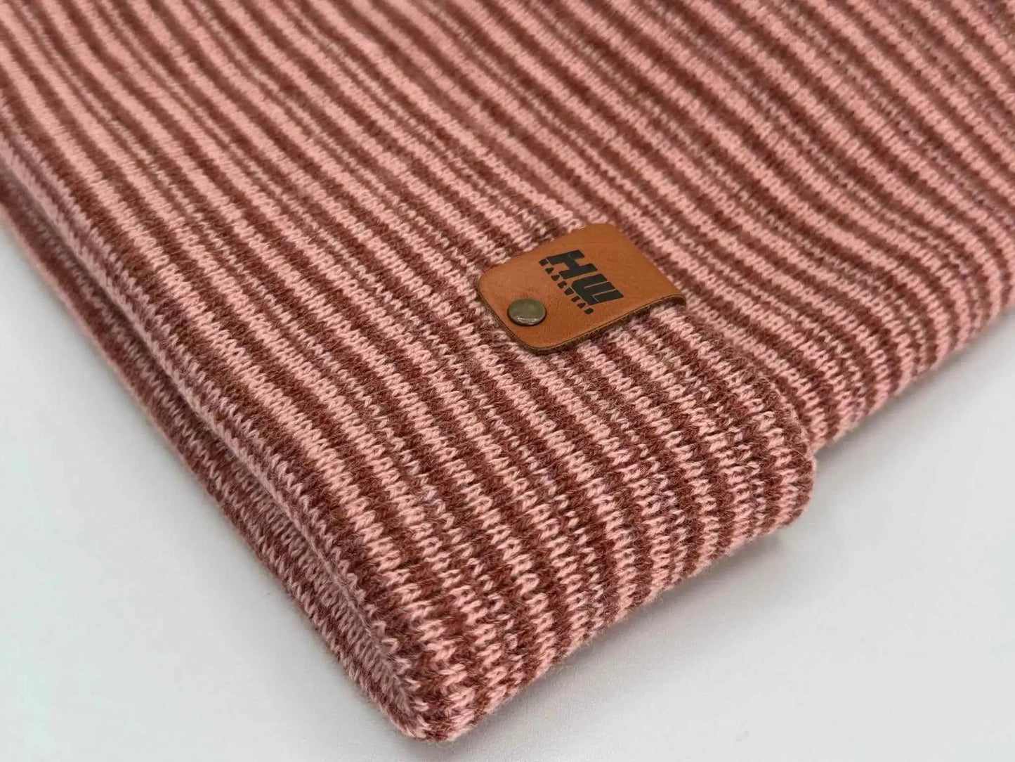 Cuffed knit beanie close-up of logo patch on burgundy-pink striped cuff
