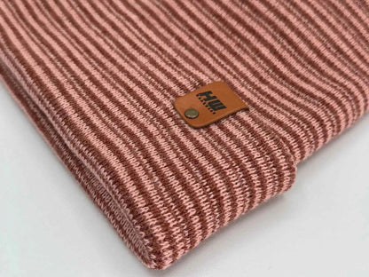 Cuffed knit beanie close-up of logo patch on burgundy-pink striped cuff