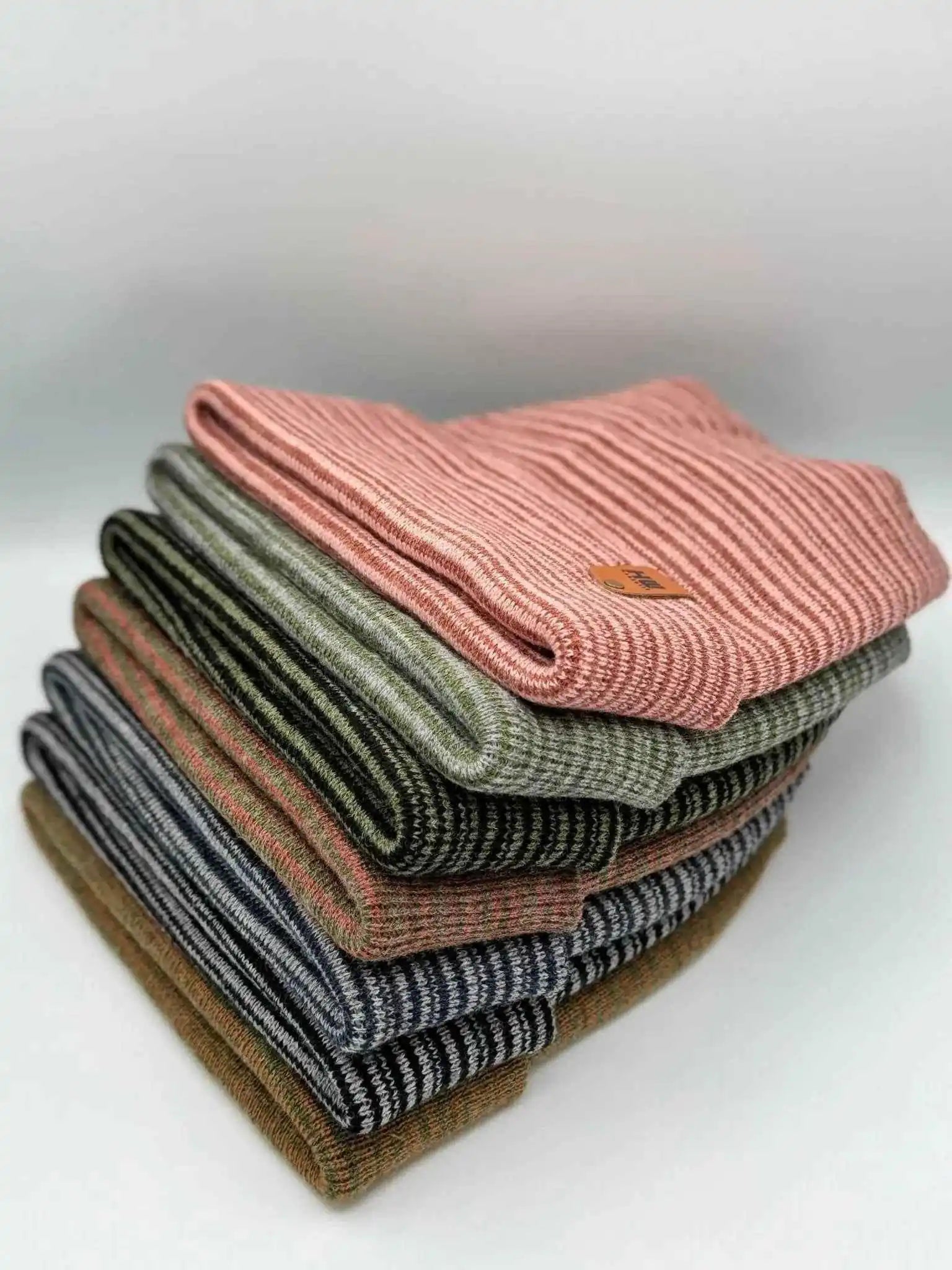 Stack of ribbed knit beanies with folded cuffs and orange logo patches, mixed colors