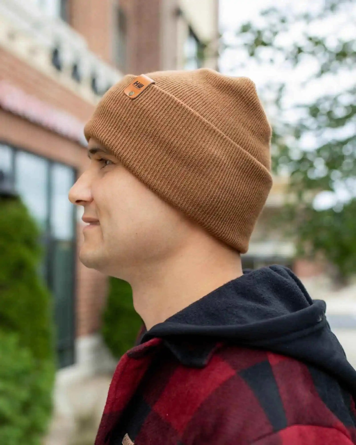 Camel brown knit beanie with folded cuff and logo patch, worn in profile