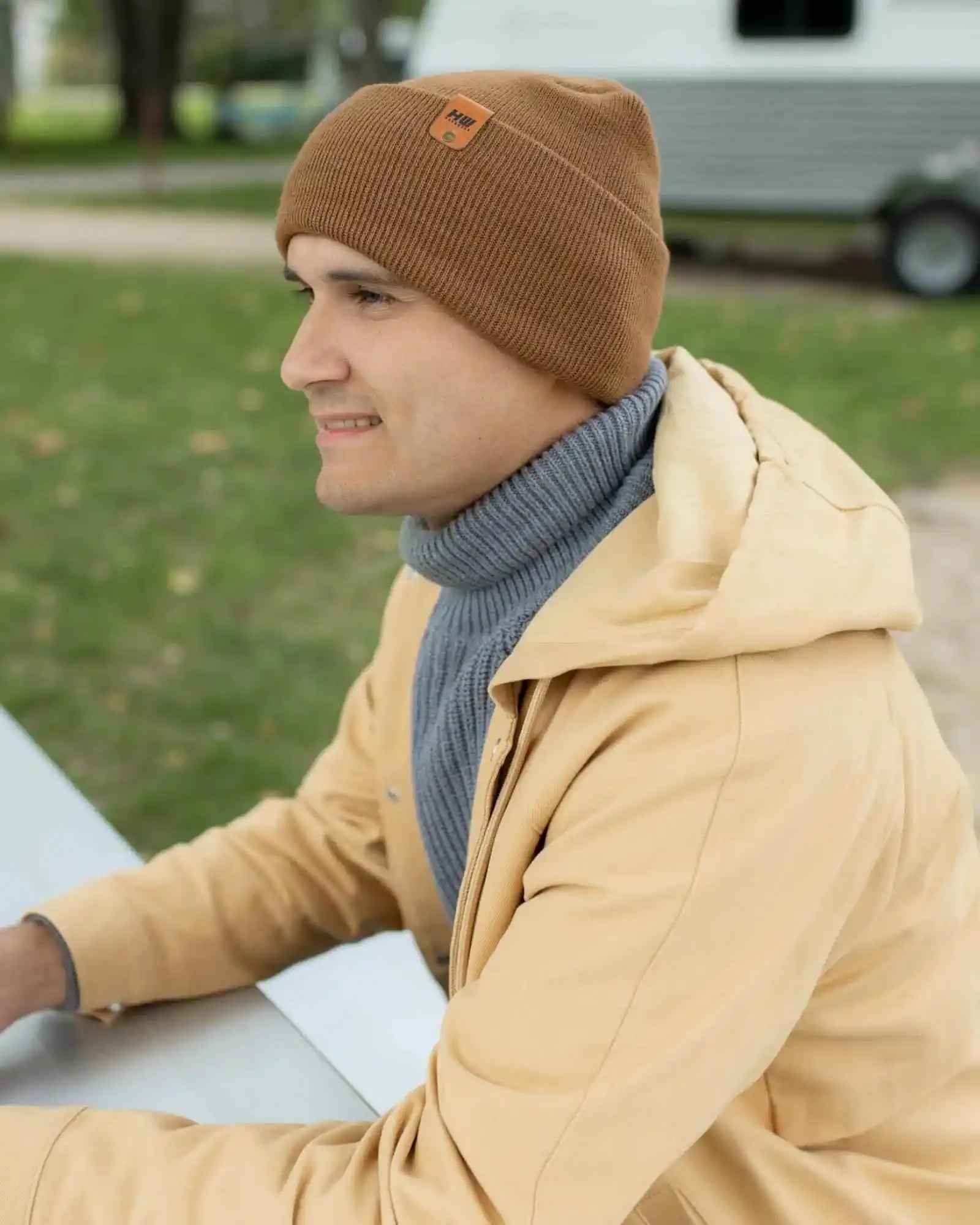 Camel brown knit beanie with folded cuff and logo patch, worn on side