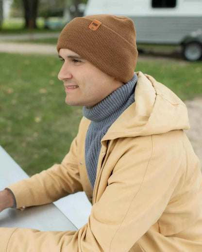 Camel brown knit beanie with folded cuff and logo patch, worn on side