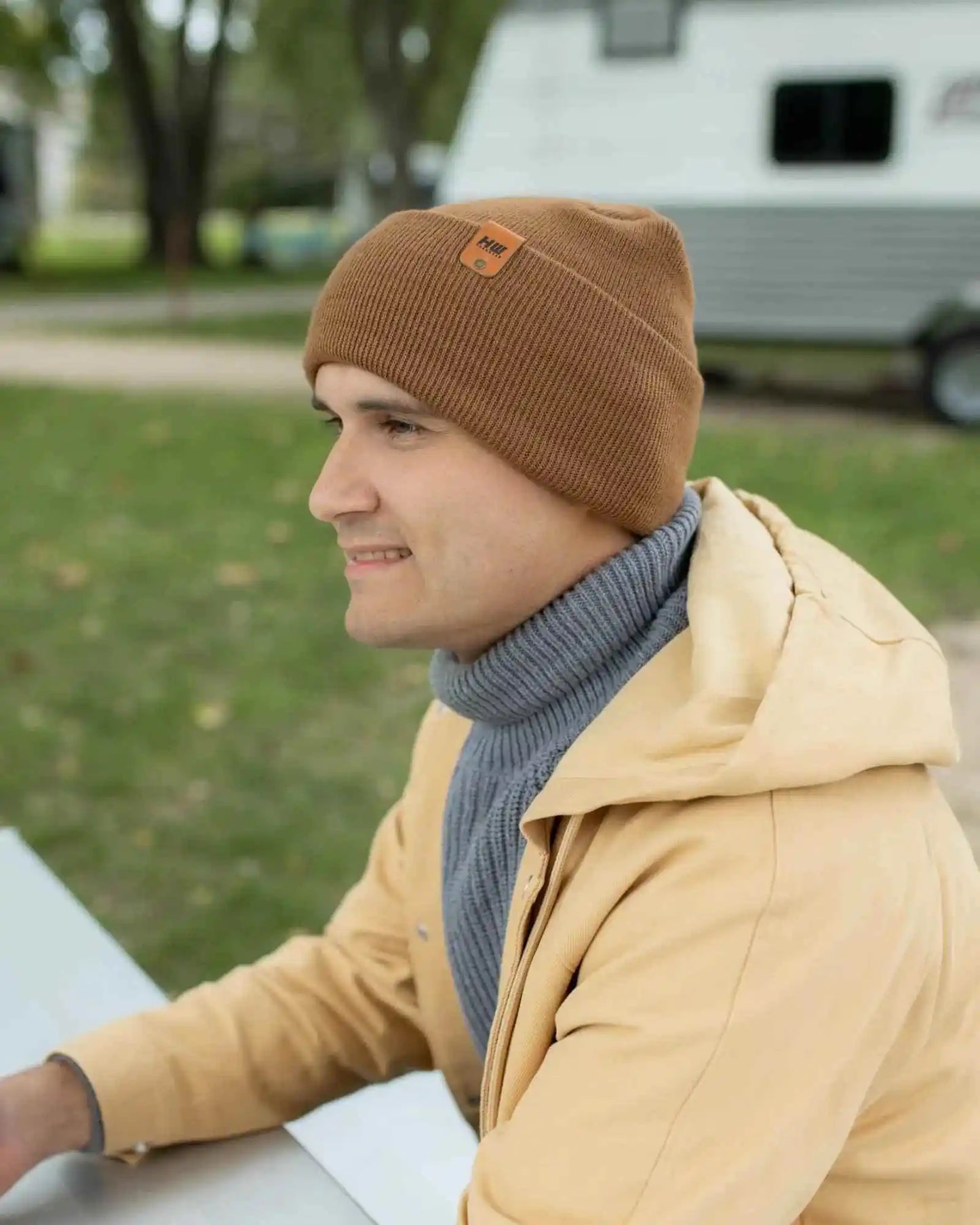 Camel brown ribbed cuff beanie with stitched front patch, worn to the side