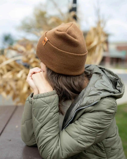 Camel brown knit beanie with turn-up cuff and front tag patch, worn back view
