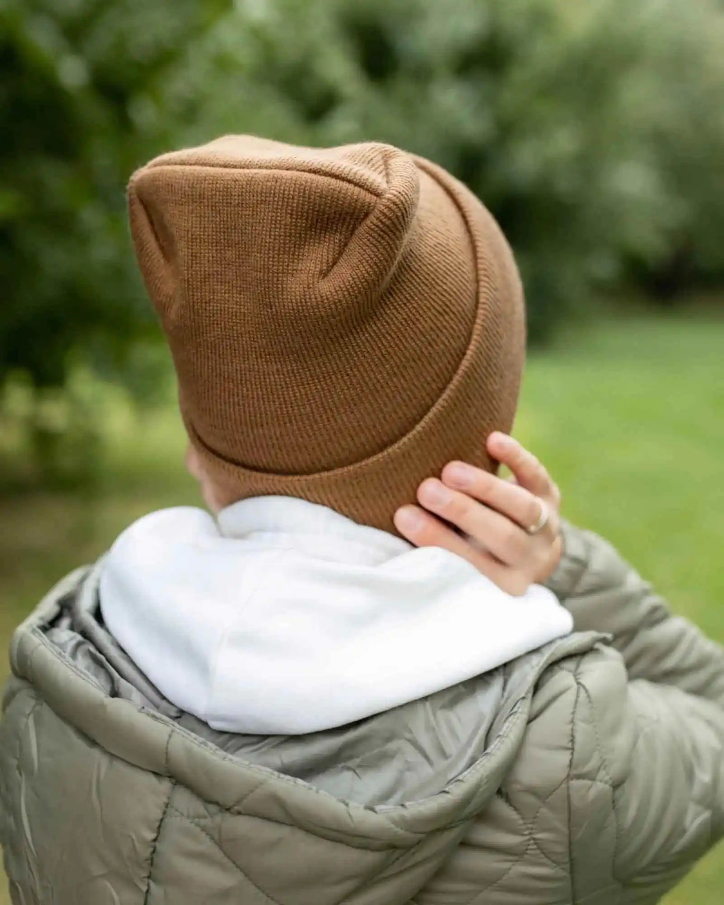 Camel brown cuffed knit beanie with stitched back panel, worn with hands to head
