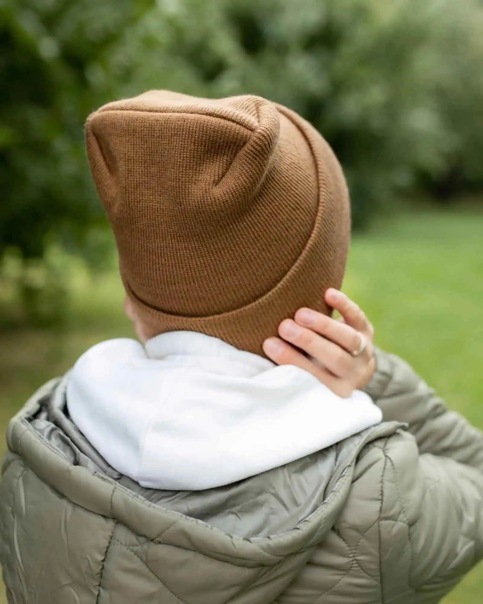 Camel brown cuffed knit beanie with stitched back panel, worn with hands to head