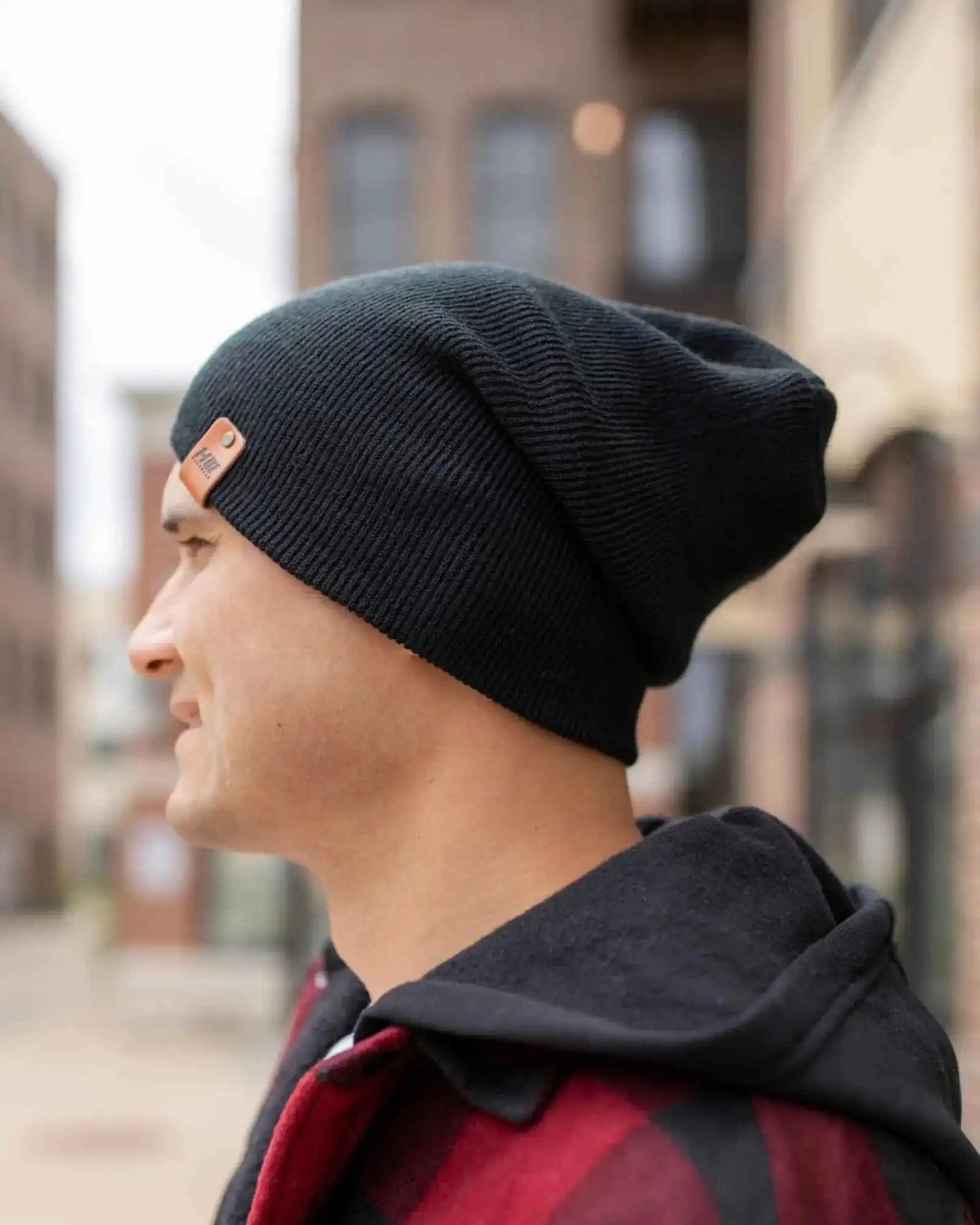 Charcoal black cuff beanie on person, profile view and small square logo patch