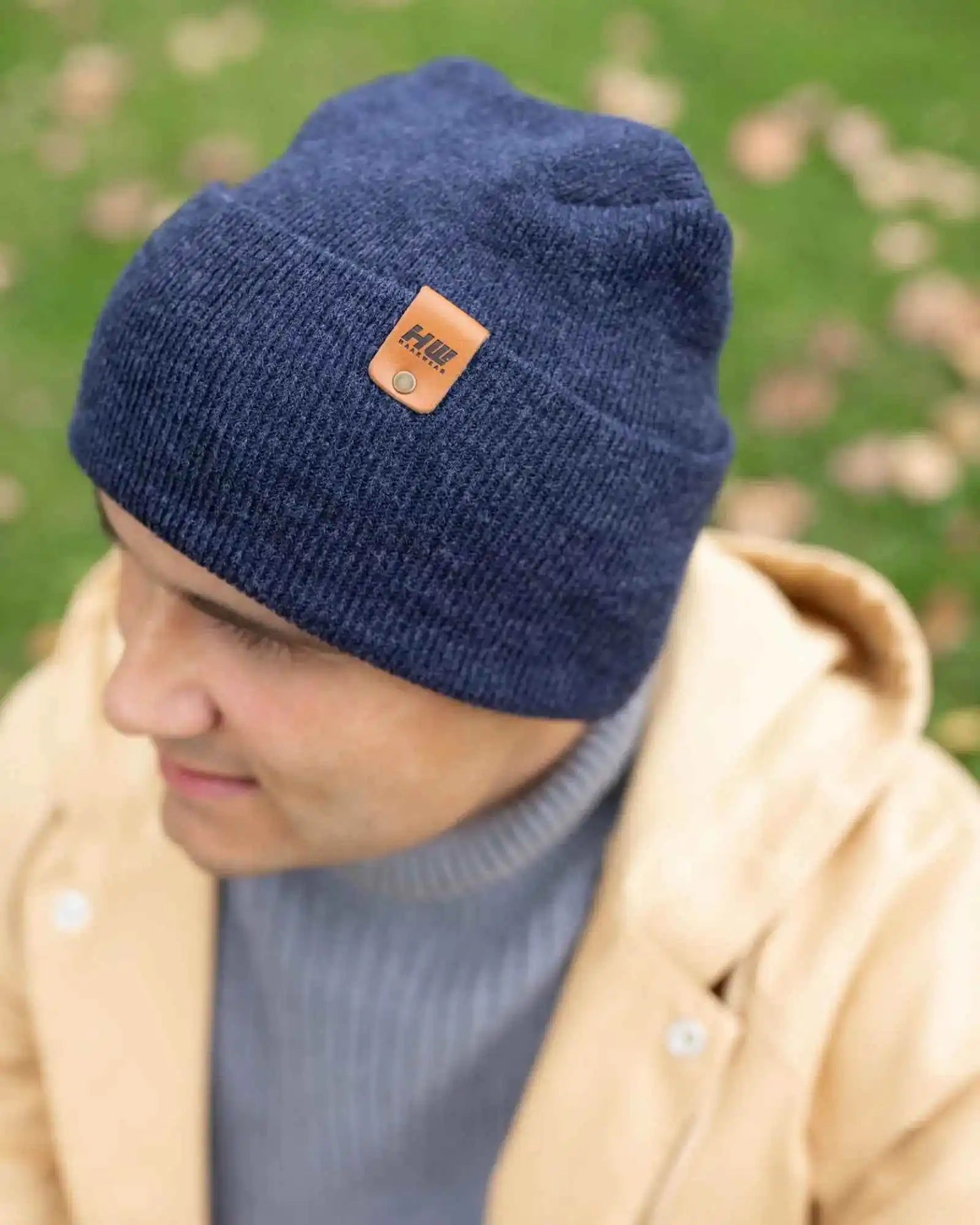 Denim blue knit beanie with tan logo patch on cuff, close side view