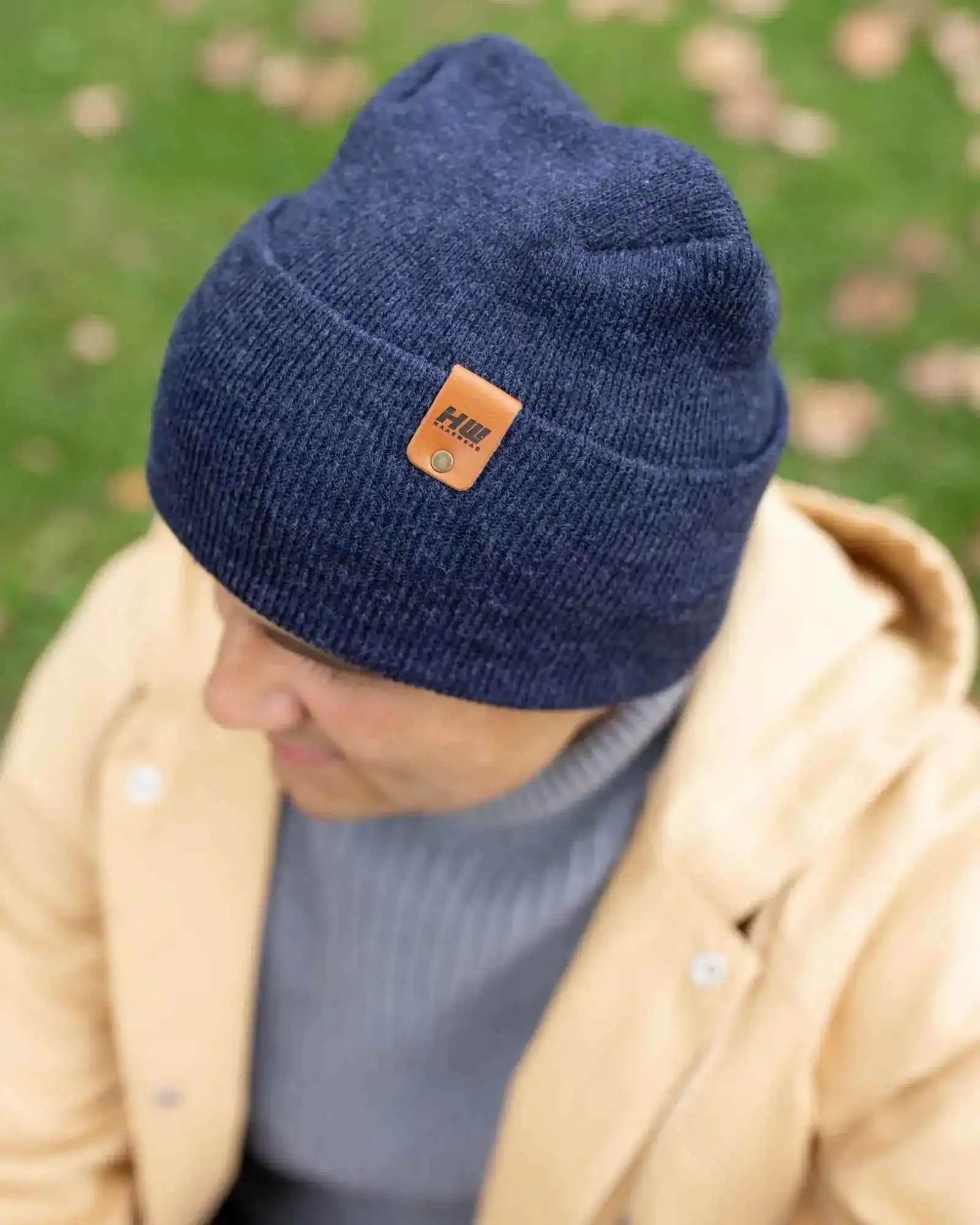 Denim blue beanie with folded cuff and tan logo patch, angled view