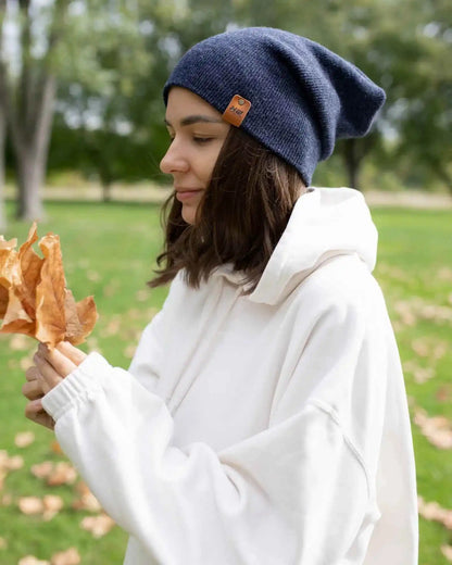 Denim blue knit beanie with tan logo patch and ribbed fold, model in white hoodie