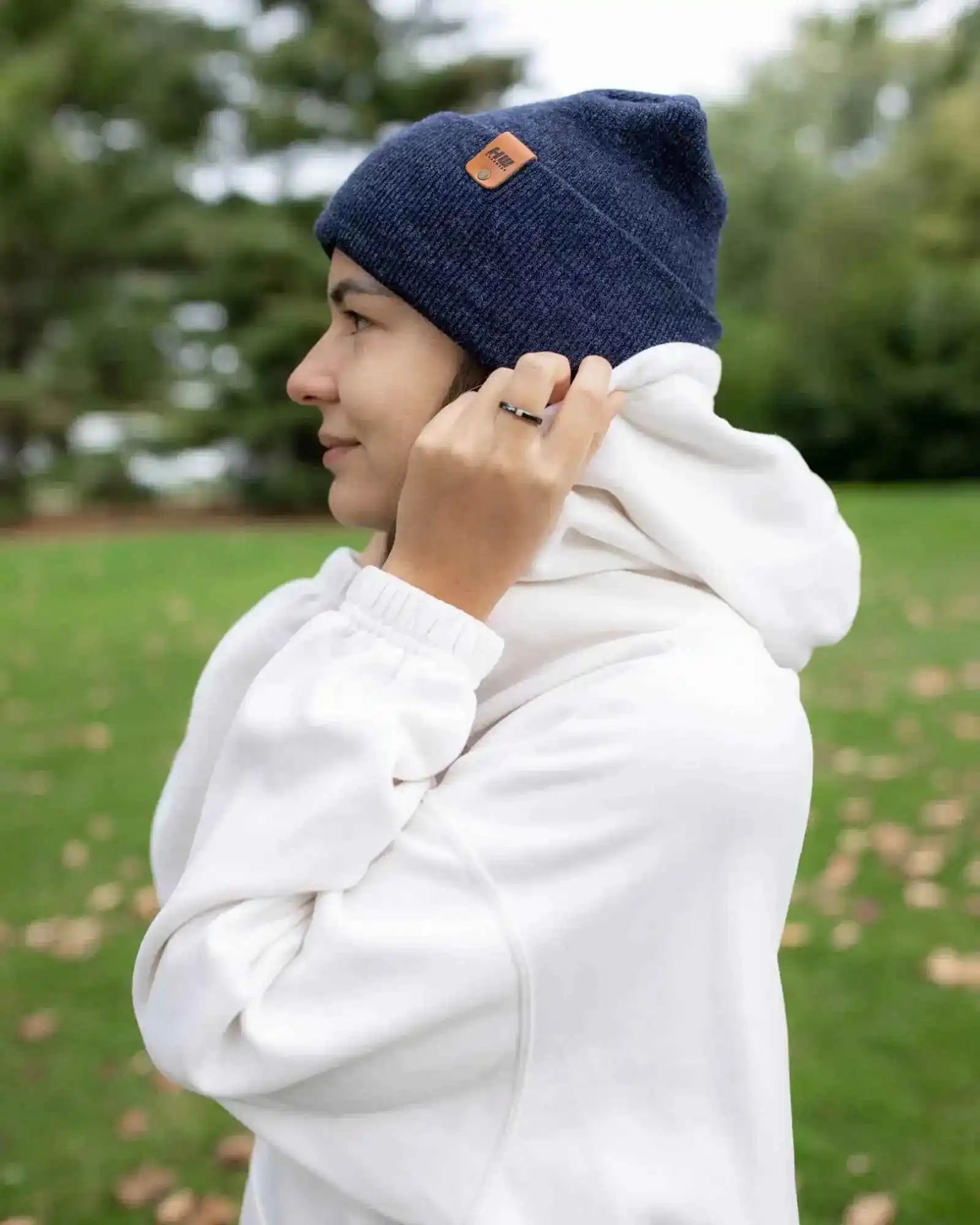Denim blue beanie with tan logo patch and ribbed cuff, model in white coat