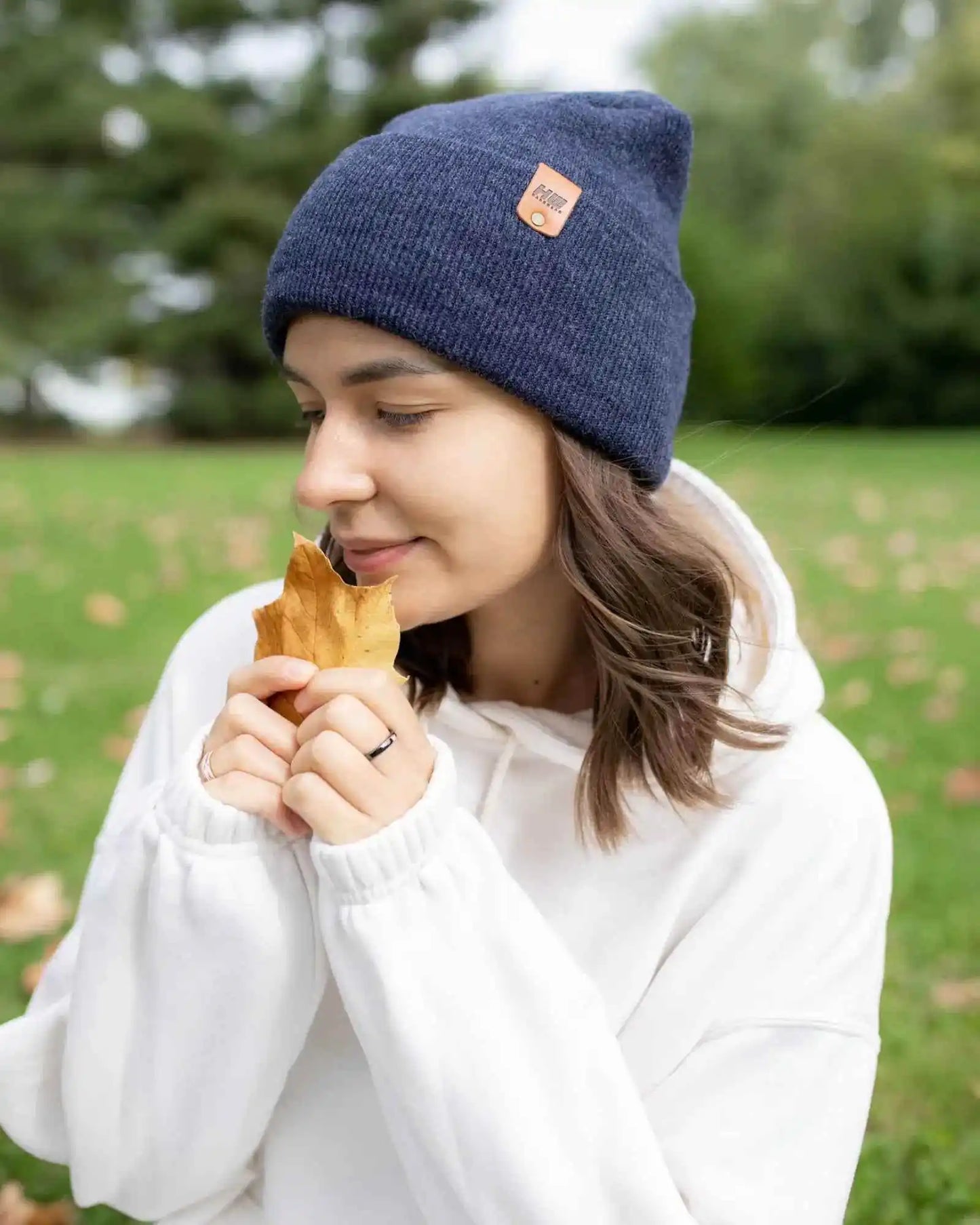 Denim blue cuffed beanie with tan logo patch, model holding leaves